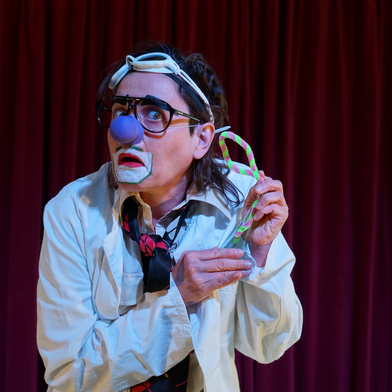 Verrückter Prof Ein Clown in einem weißen Kittel zeigt eine bunte Süßigkeit mit einem verwirrten Ausdruck.